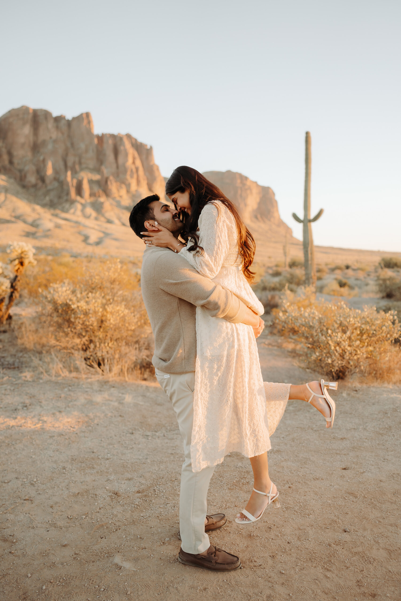 A guy picking up the girl almost kissing in front of Superstition Mountains at Lost Dutchman State Park in Arizona.