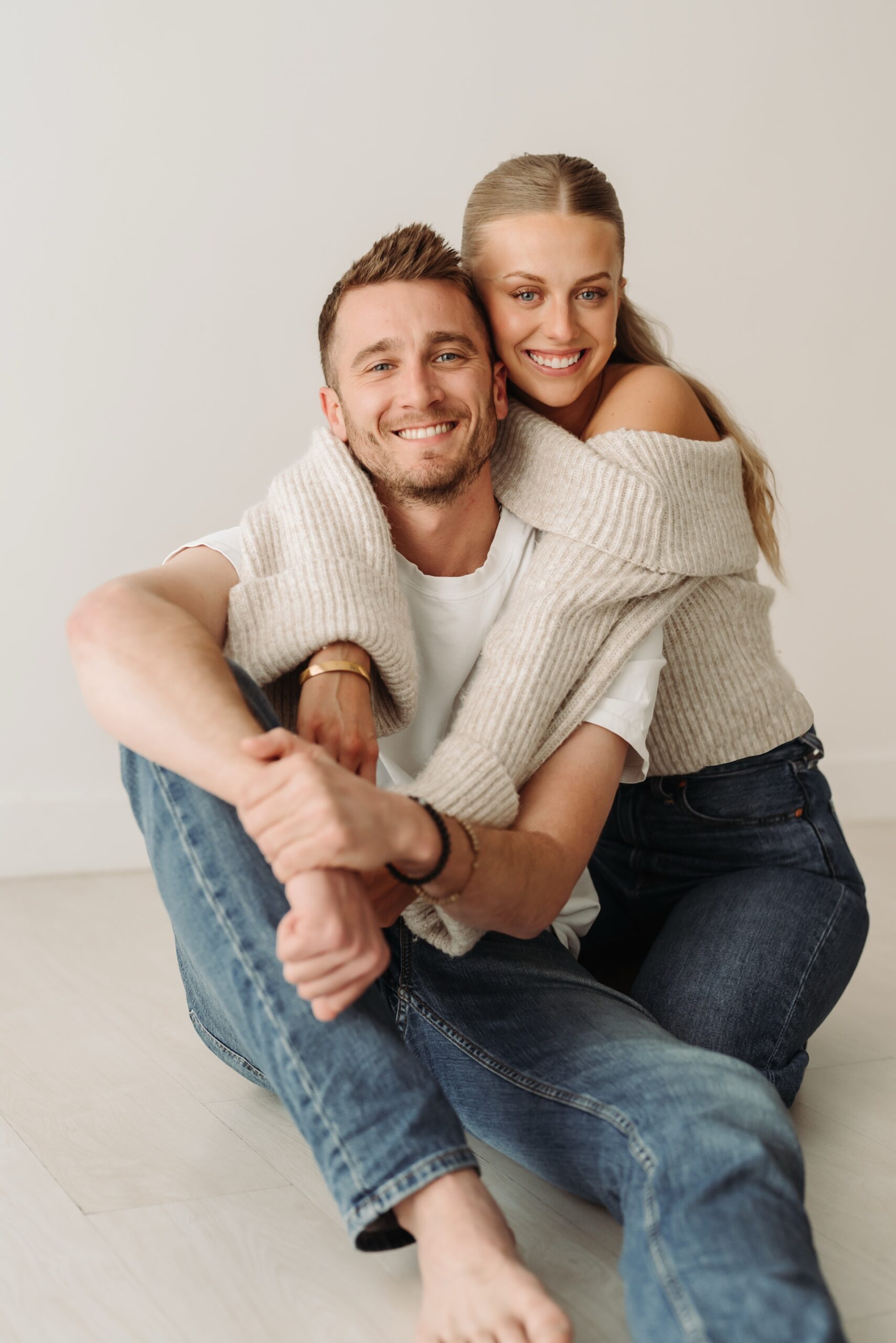 Girl is hugging boyfriend from behind while sitting on the floor.